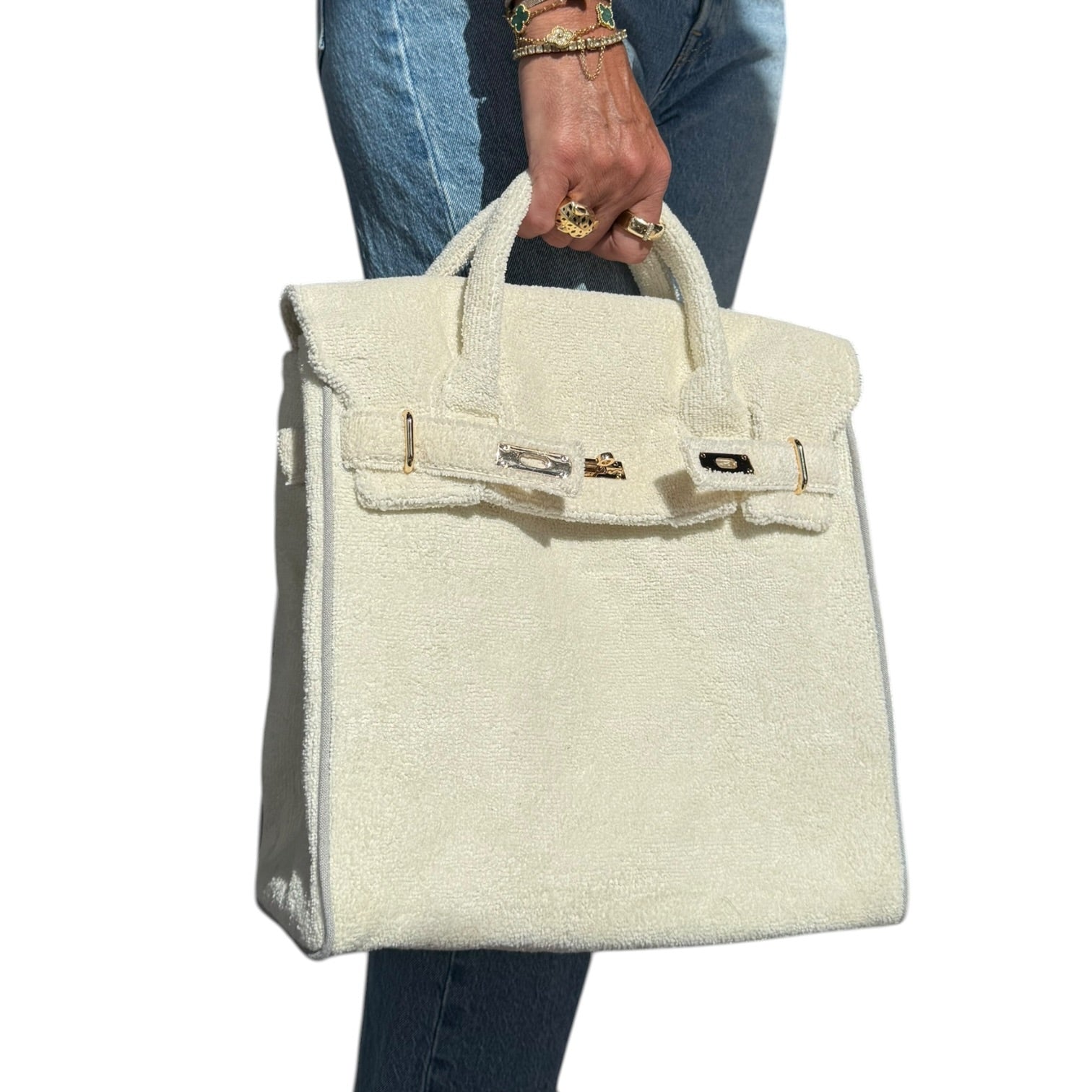 off white handbag held by a person wearing blue jeans on a white background