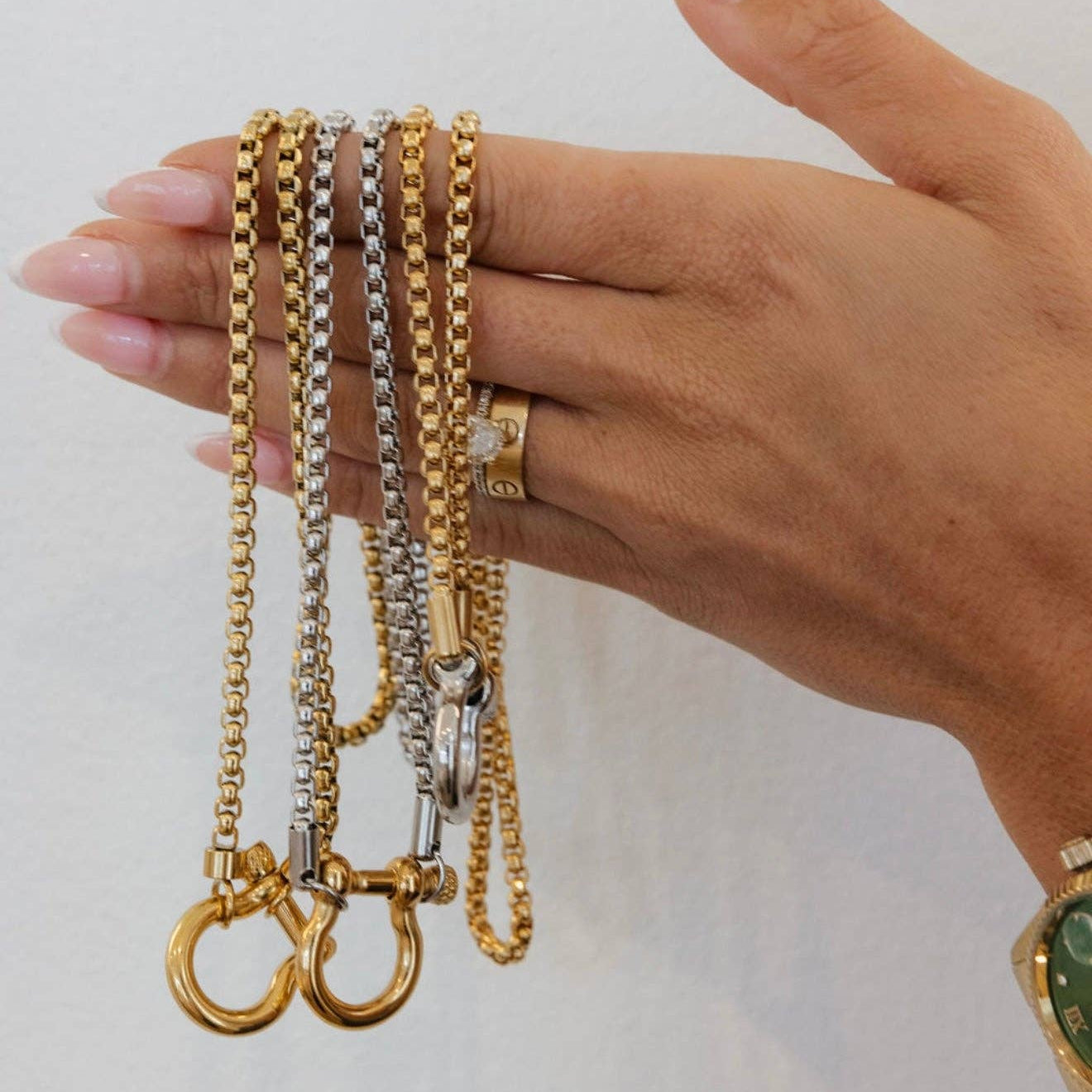 Hand holding three gold and silver chains against a plain background