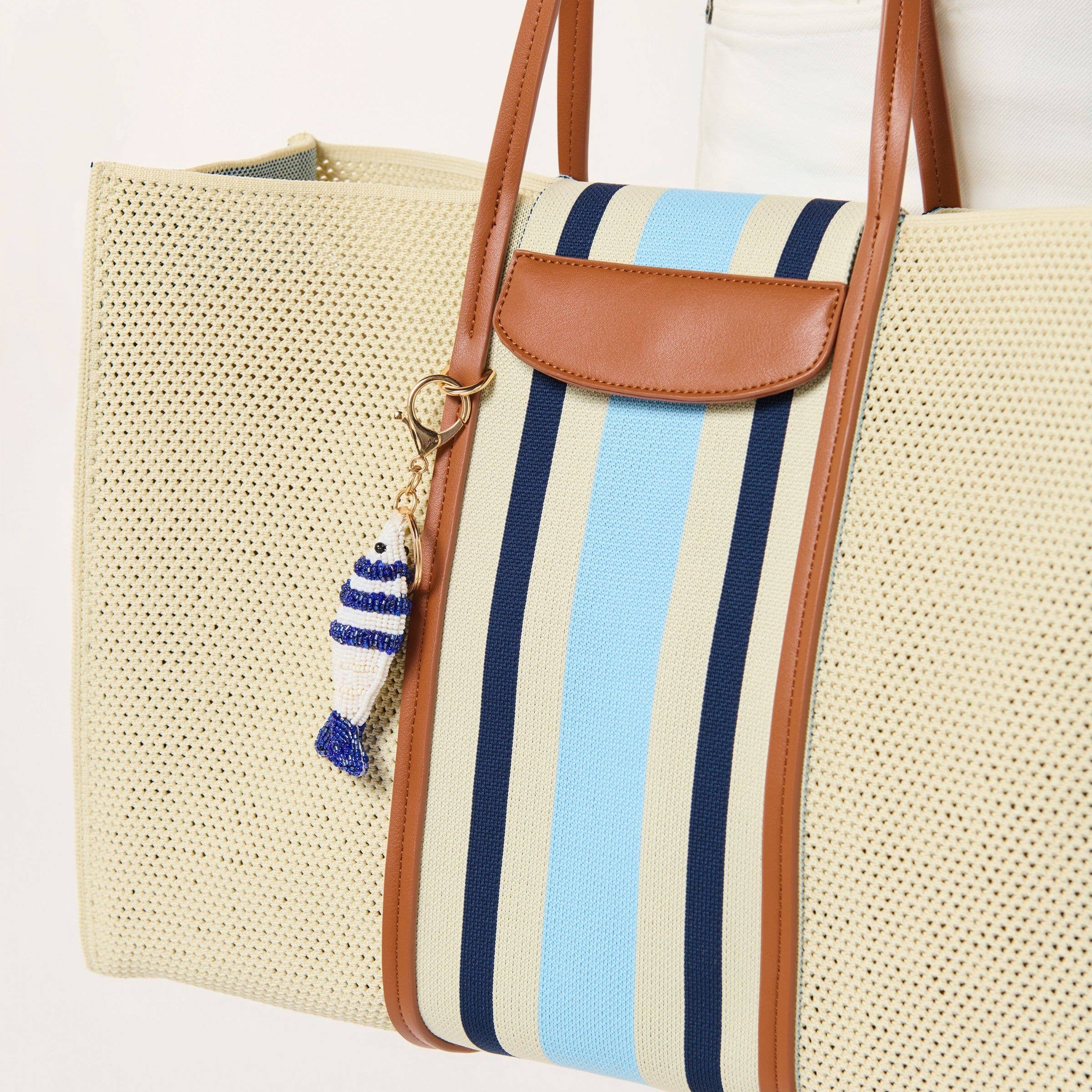 Beige woven tote bag with blue and white striped section and brown leather handle and flap.