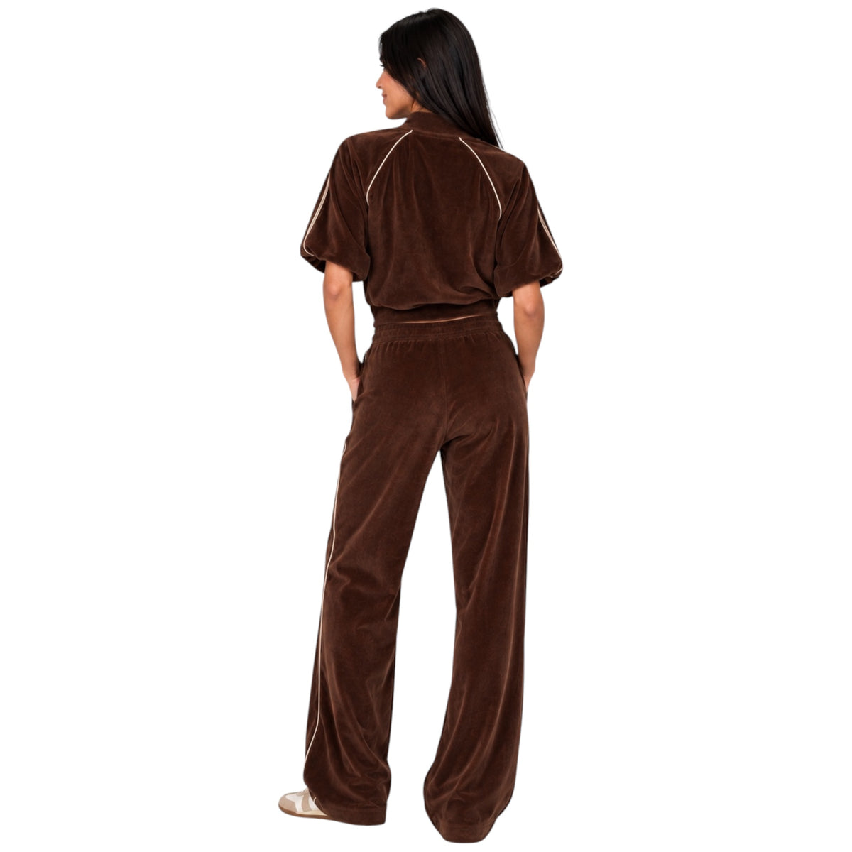 A woman wearing a matching brown velour tracksuit, viewed from behind, standing against a solid white background.