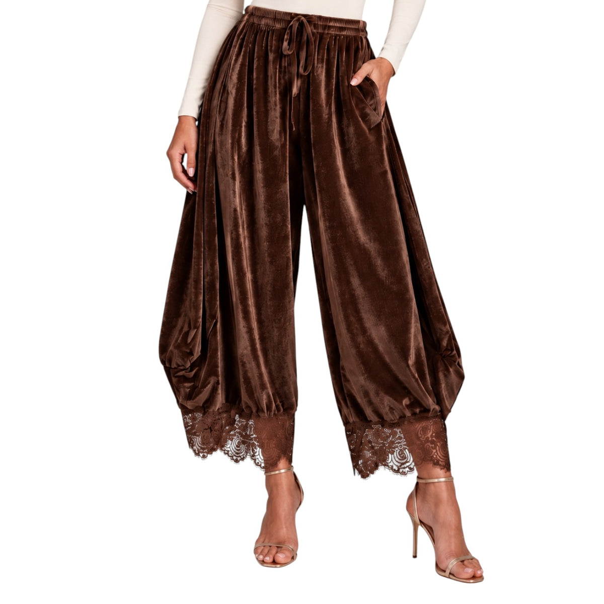 A model wears high-waisted, wide-leg brown velvet harem pants with a drawstring waist, side pockets, and lace trim at the hems, paired with a cream long-sleeve top and clear high-heeled sandals against a white background.