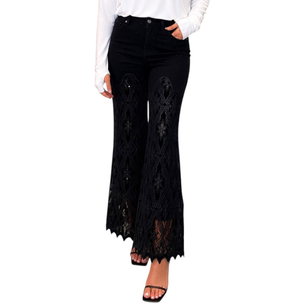Black wide-leg flare pants with intricate lace panels on the front, shown on a model wearing a white long-sleeve top and black sandals against a white background.