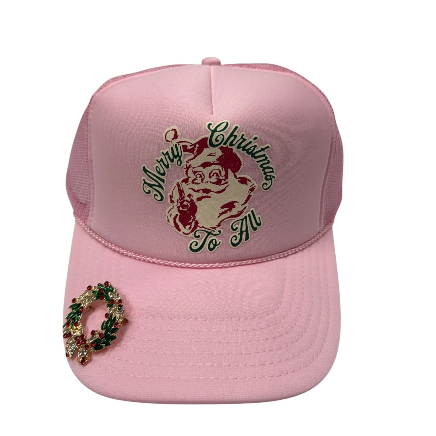 A light pink trucker hat with a Santa Claus graphic on the front reading 'Merry Christmas To All' in green and gold, and a green and gold wreath embellishment on the brim.