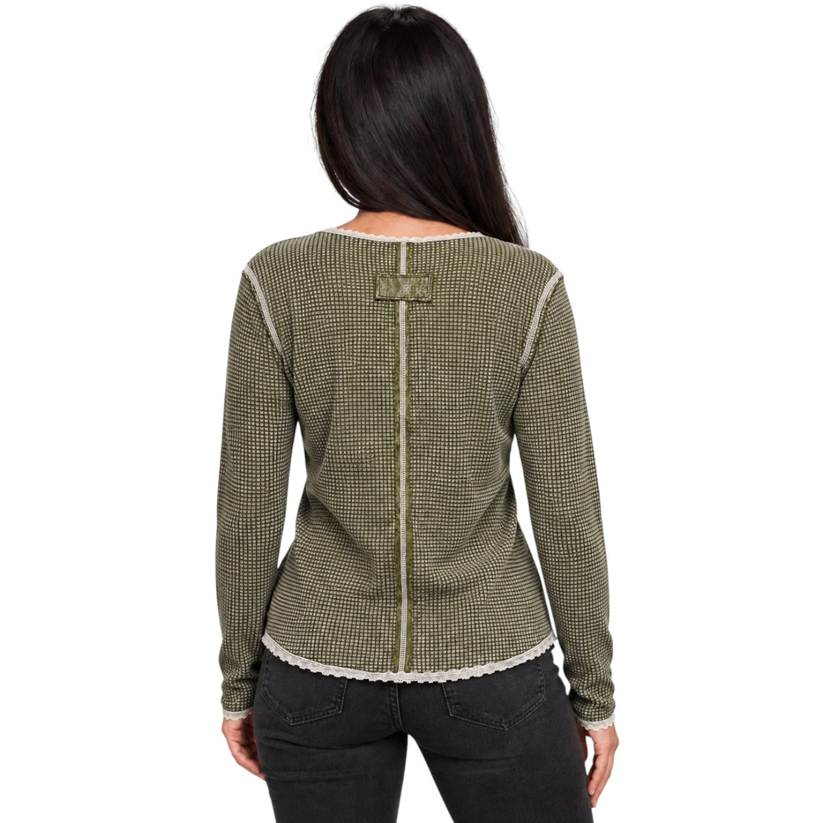 A woman viewed from the back wearing a textured olive green and black houndstooth knit sweater with cream-colored trim and a decorative button detail at the back neckline, paired with black jeans against a plain white background.
