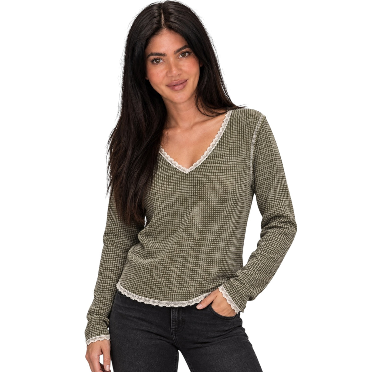 A woman modeling a long-sleeve knit sweater with a small-scale green and beige houndstooth pattern and white lace trim along the V-neck, cuffs, and hem, paired with black jeans against a solid white background.