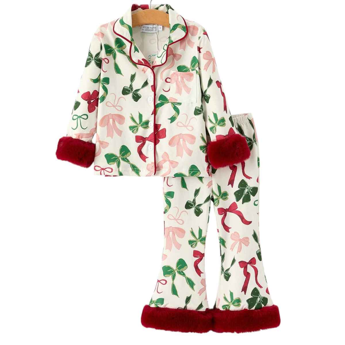 A two-piece pajama set featuring a long-sleeve top and matching pants with an off-white background, decorated with a festive pattern of pink bows, green ivy, and red ribbons. The cuffs and hem of the top and pants are finished with plush red trim.