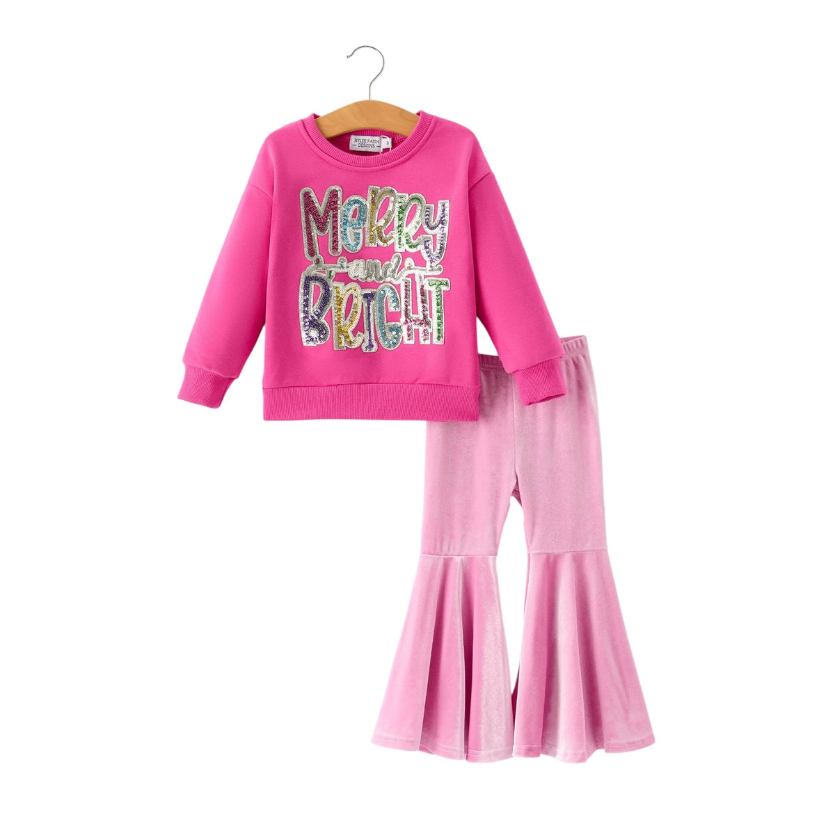 A two-piece girls' outfit set in bright pink, featuring a long-sleeve sweatshirt with a colorful 'Merry and Bright' text graphic and matching pink flared pants, displayed on a wooden hanger against a white background.