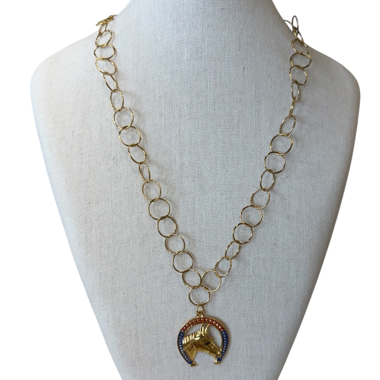 A gold-tone chain necklace with a horse-head pendant, displayed on a cream fabric-covered jewelry bust against a white background.