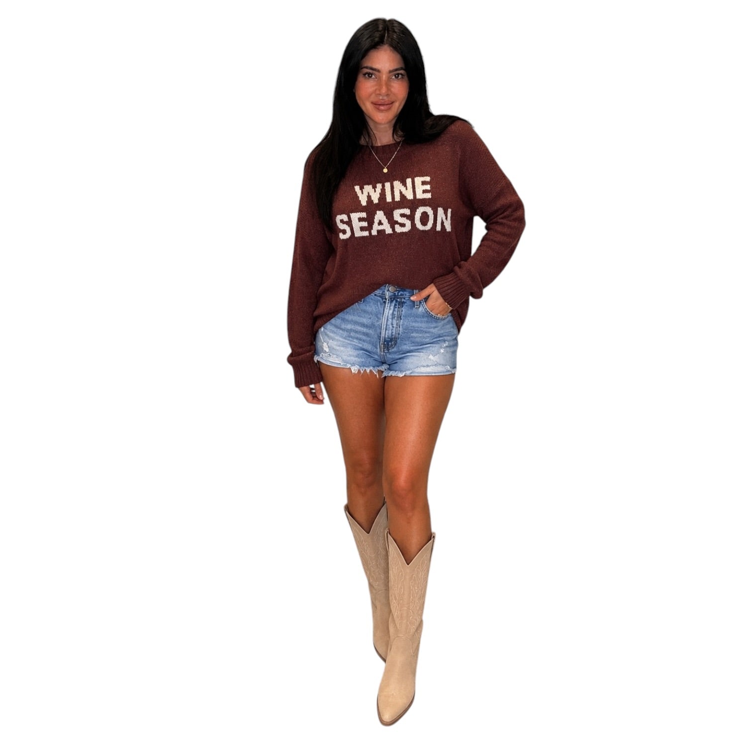 A woman modeling a brown long-sleeve sweatshirt with 'WINE SEASON' printed in beige across the chest, paired with denim shorts and beige cowboy boots, on a plain white background.