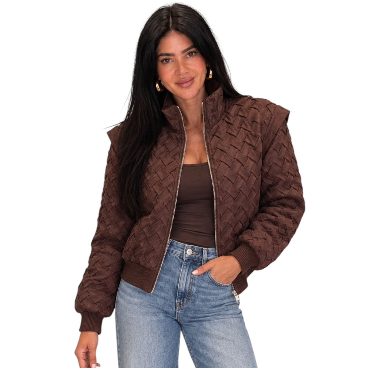 A woman wearing a brown quilted bomber jacket with a textured basketweave pattern, styled with a matching brown top and blue jeans against a plain white background.