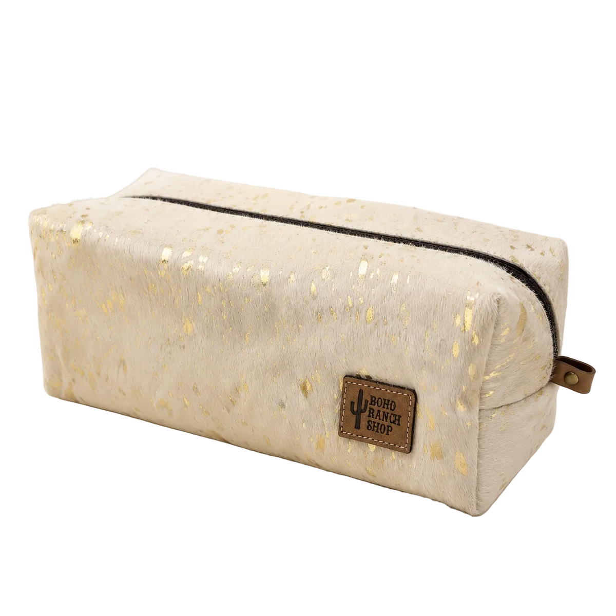 A cream-colored zippered pouch with gold foil speckles, featuring a brown leather patch with the brand name 'UNIQUE RANCH SHOP' and a black zipper, set against a clean white background with dried pampas grass in the corner.