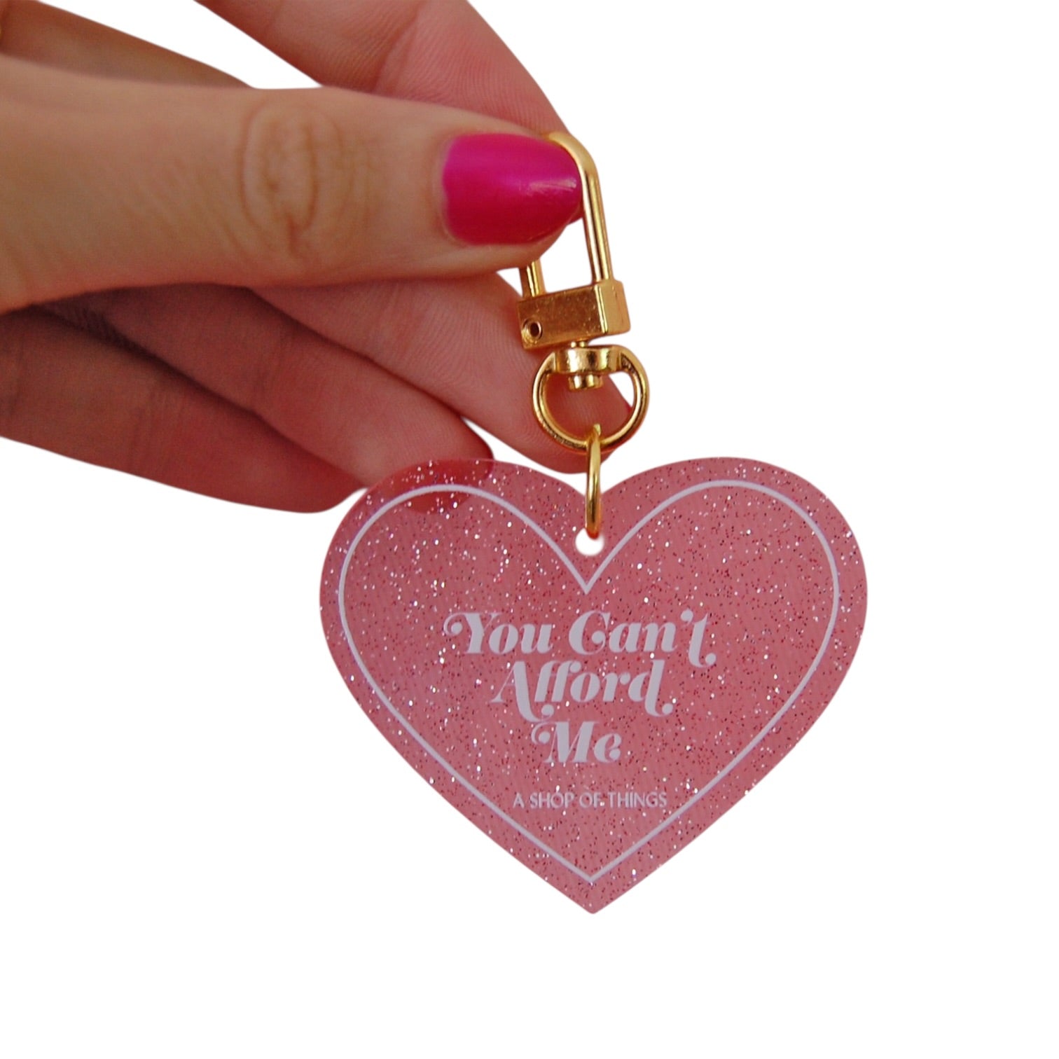 Heart-shaped keychain with 'You Can't Afford Me' text held by a hand with pink nail polish.