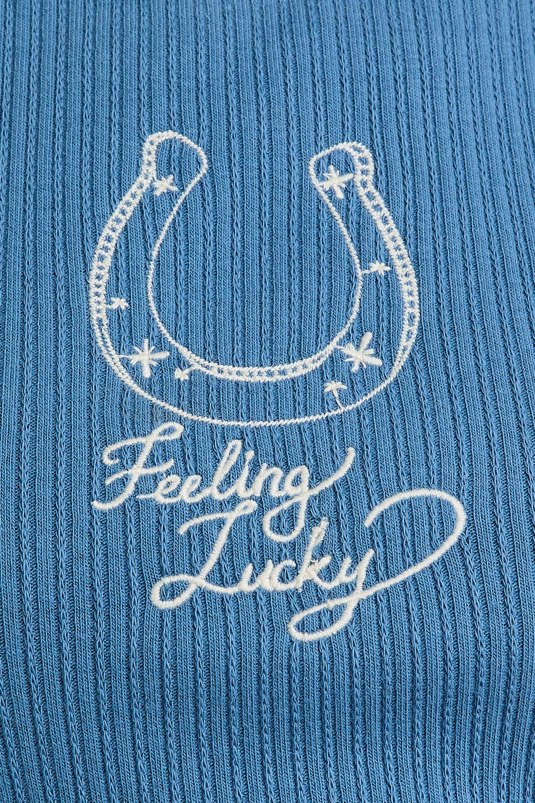 Embroidery detail of a horseshoe and 'Feeling Lucky' text on a dusty blue rib tank top.