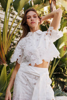 Elegant woman in a floral lace cropped blouse set against tropical foliage, showcasing modern femininity.