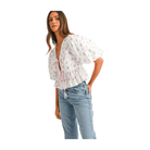 Model wearing a pink and white floral bow crop top with peplum style and puff sleeves, paired with denim jeans.