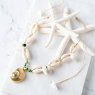 Elegant snail shell necklace with gold accents and beads, set against starfish on marble background.