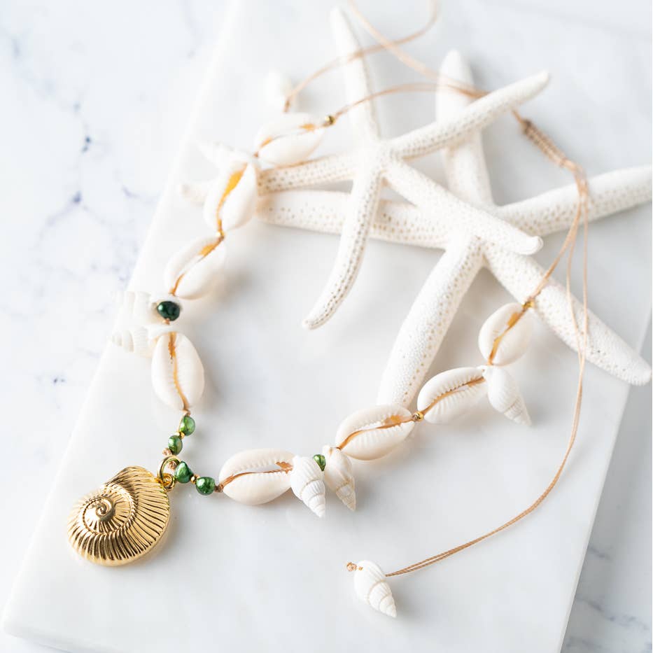 Elegant snail shell necklace with gold accents and beads, set against starfish on marble background.