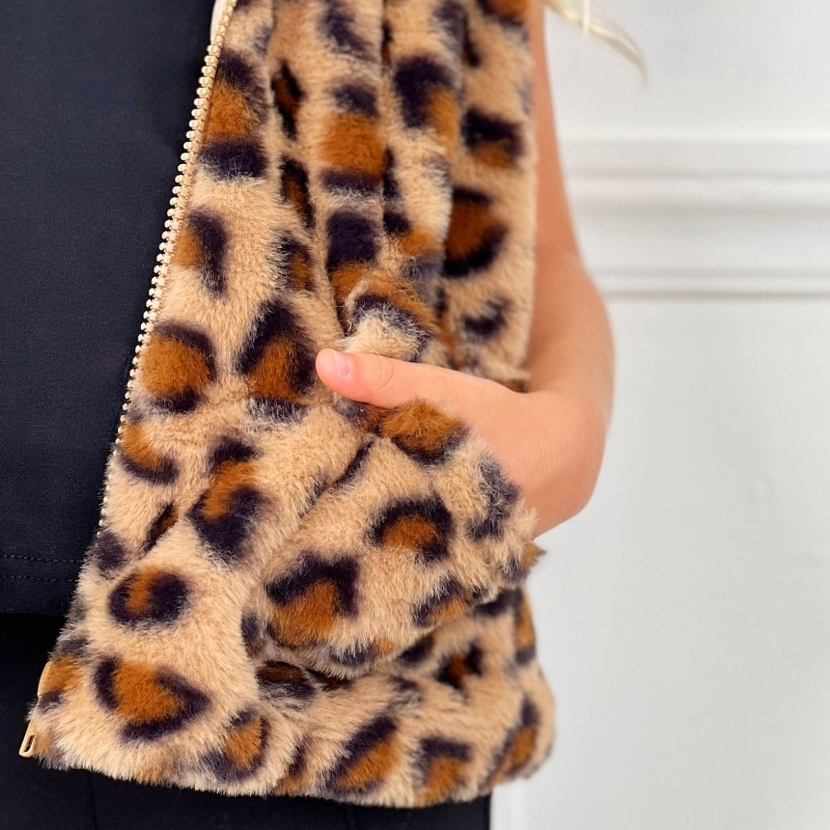 Leopard print fur vest held by a person against a neutral background