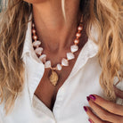 Gold large shell statement necklace in salmon pink, styled with a white shirt, perfect for summer beach outfits.