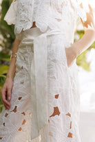 Model showcasing floral lace belted pants set with sheer blouse and flowing lace details in an elegant outdoor setting.