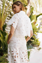 Elegant woman in floral lace belted pants set, showcasing delicate crochet details in a lush outdoor setting.