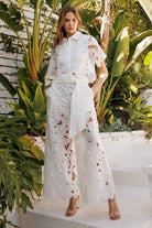 Model in floral lace belted pants set against tropical greenery, showcasing elegance and modern femininity.