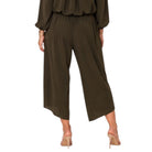 A woman viewed from the back wearing an olive green two-piece jumpsuit with a long-sleeve draped top and wide-leg cropped pants, paired with nude high heels against a plain white background.