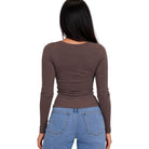 A woman viewed from the back wearing a fitted, long-sleeve brown top and light blue jeans against a plain white background.