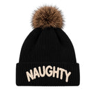 A black ribbed knit beanie hat with a brown faux fur pom-pom on top and the word 'NAUGHTY' embroidered in cream across the front cuff, shown on a plain white background.