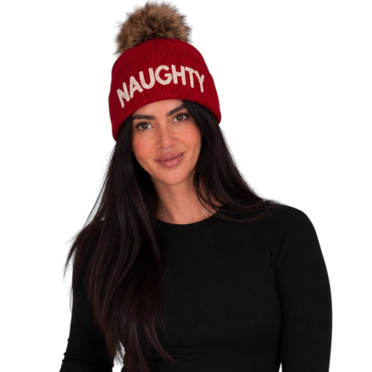 A woman wearing a red knit beanie with a brown faux-fur pom-pom and the word 'NAUGHTY' in white capital letters on the front, against a plain white background.