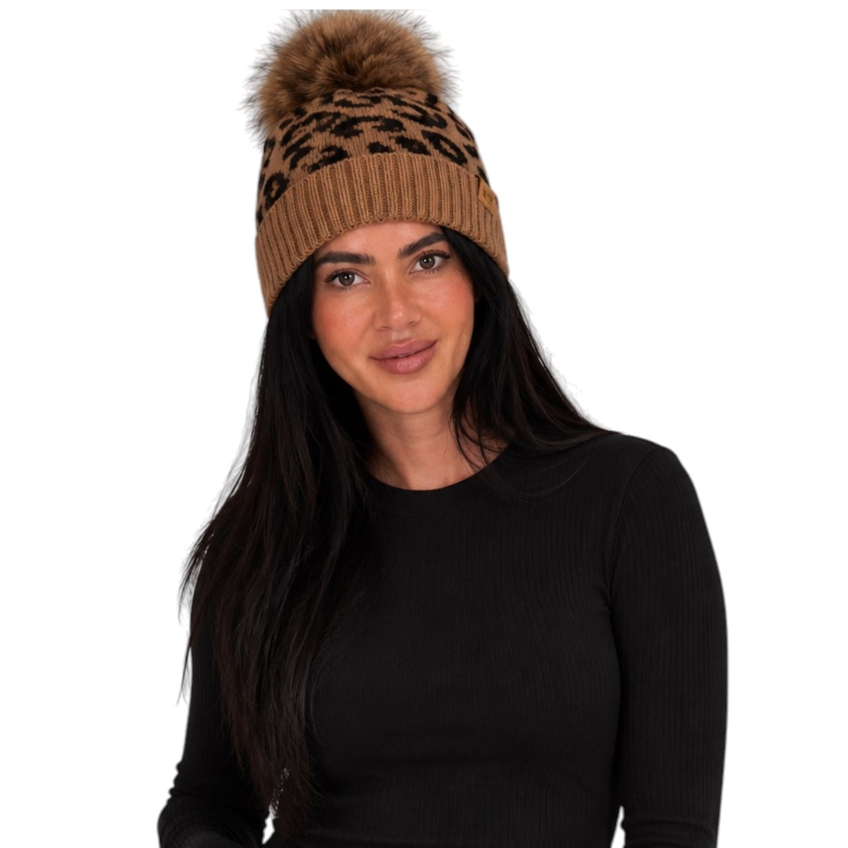 A woman with long dark hair wearing a brown and black leopard-print knit beanie with a matching faux-fur pom-pom, paired with a black ribbed long-sleeve top, against a plain white background.