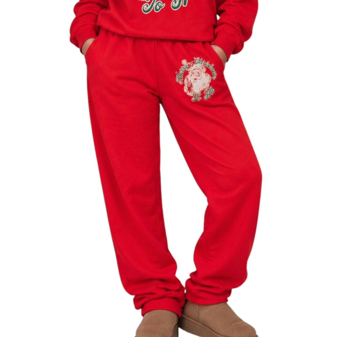 A person wearing a red holiday sweatshirt and matching sweatpants with a Santa graphic on the thigh, paired with tan boots, against a plain white background.