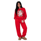 A woman modeling a red Christmas-themed sweatshirt and jogger pants set. The sweatshirt features a large graphic of Santa Claus with 'Merry Christmas' written in green and white.
