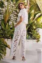 Model wearing floral lace belted pants set, featuring delicate crochet lace and a chic sheer blouse in a tropical setting.