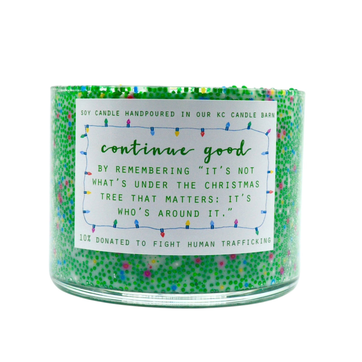 A green jar candle with colorful glitter and a white paper label that reads 'continue good' with a human trafficking awareness message, on a plain white background.