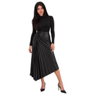 A woman modeling a black long-sleeve mock-neck top paired with a black pleated faux-leather midi skirt and black pointed-toe heels, set against a plain white background.