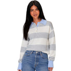 A woman modeling a light blue and white striped knit polo sweater with a light blue collar and cuffs, paired with blue jeans, against a plain white background.