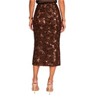 A model shown from the back wearing a brown sequined midi skirt, nude heels, and gold bracelets against a plain white background.