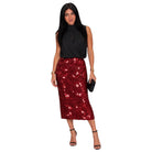 A woman modeling a sleeveless black top and a red sequined midi skirt, holding a small black clutch against a plain white background.