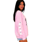 A woman wearing a light pink crewneck sweatshirt with white dog graphics on the sleeve, paired with denim shorts, shown against a plain white background.