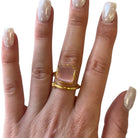 Gold ring with a clear stone on a hand with light nail polish against a white background