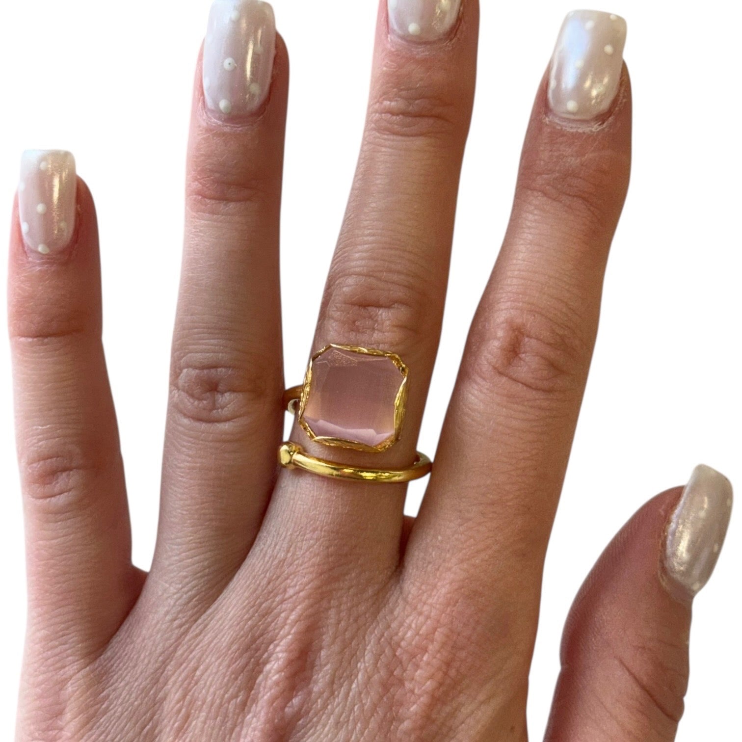 Gold ring with a clear stone on a hand with light nail polish against a white background