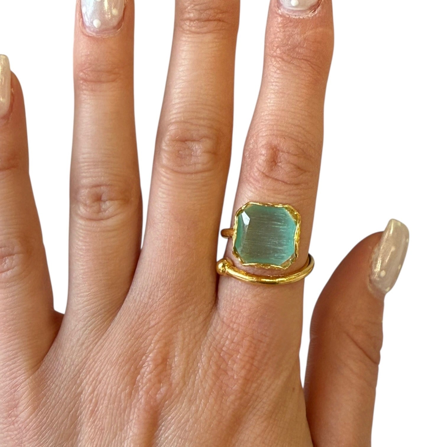 Gold ring with a green gemstone on a hand against a white background
