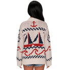 A woman viewed from the back wearing a chunky knit cardigan with a nautical design featuring red and navy blue sailboats and waves on an off-white background.