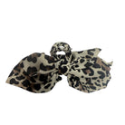 A leopard print hair bow accessory featuring a beige background with black and brown spots, photographed on a solid white background.