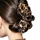 A leopard print hair claw clip styled in a braided bun on a model's hair, shown against a plain white background.