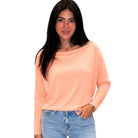 Woman wearing a peach long-sleeve top and blue jeans on a white background