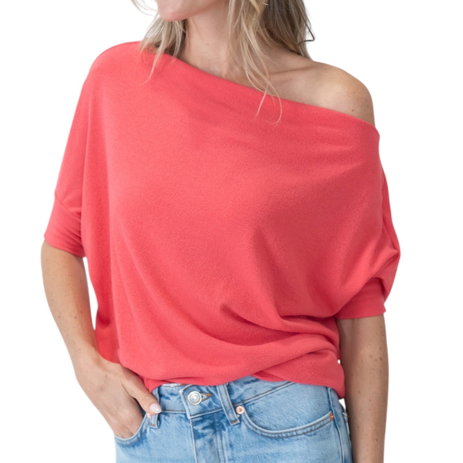Person wearing a coral off-shoulder top and blue jeans on a white background