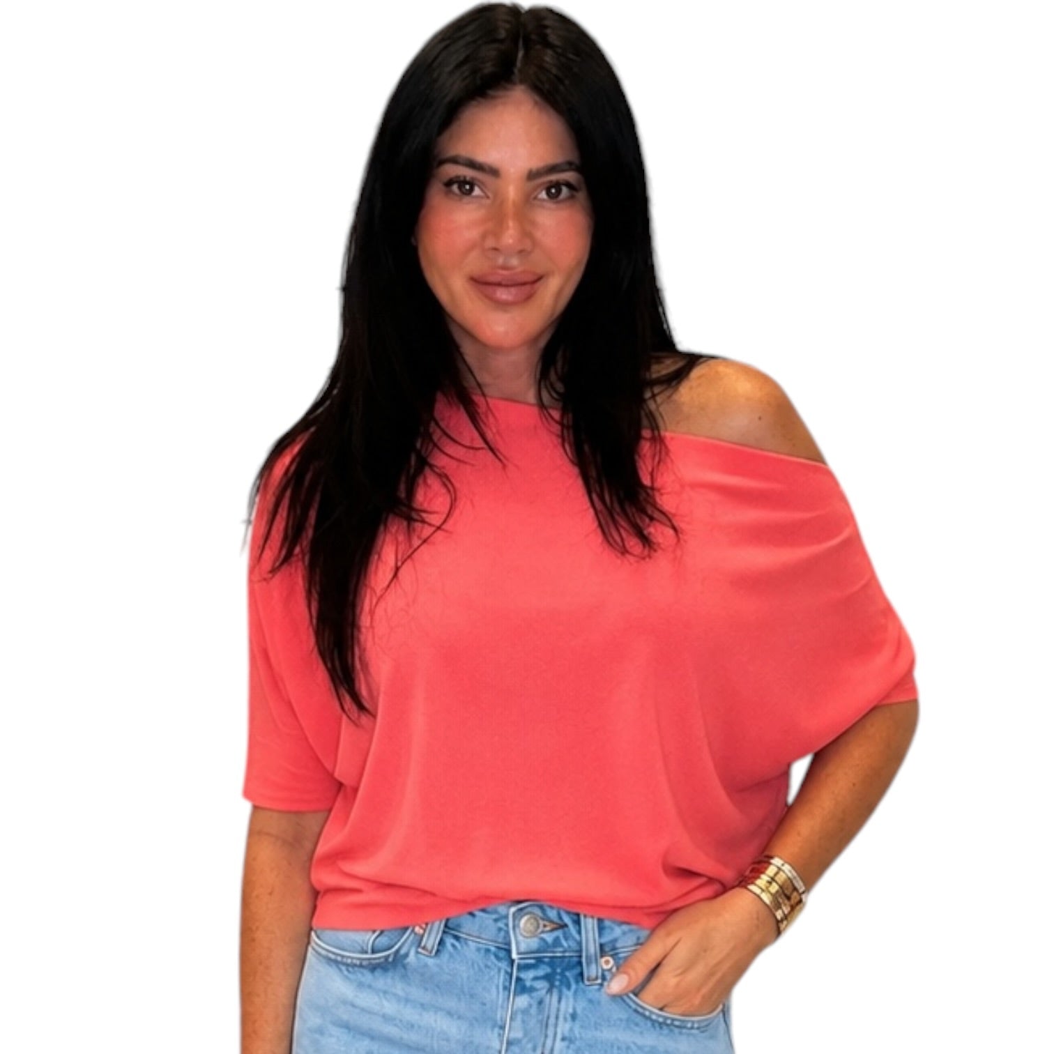 Woman wearing a coral off-shoulder top and blue jeans on a white background