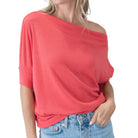Person wearing a coral off-shoulder top and blue jeans on a white background